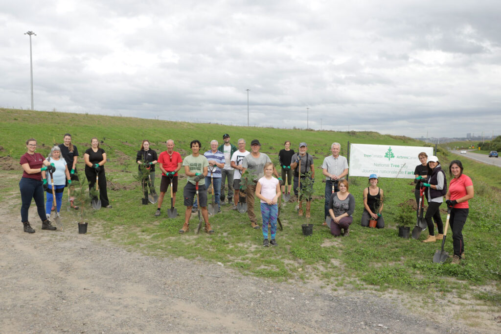 Group of tree planters standing with shovels on a field of grass in front of a National Tree Day sign.