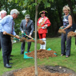 http://Group%20of%20dignitaries%20holding%20mulch%20in%20their%20shovels,%20standing%20around%20a%20newly%20planted%20tree.
