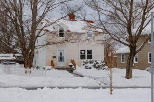 House and trees on snow covered street.