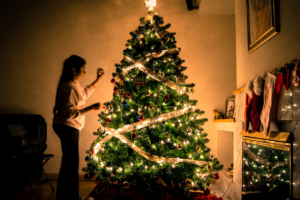 young woman decorating large lit up christmas tree