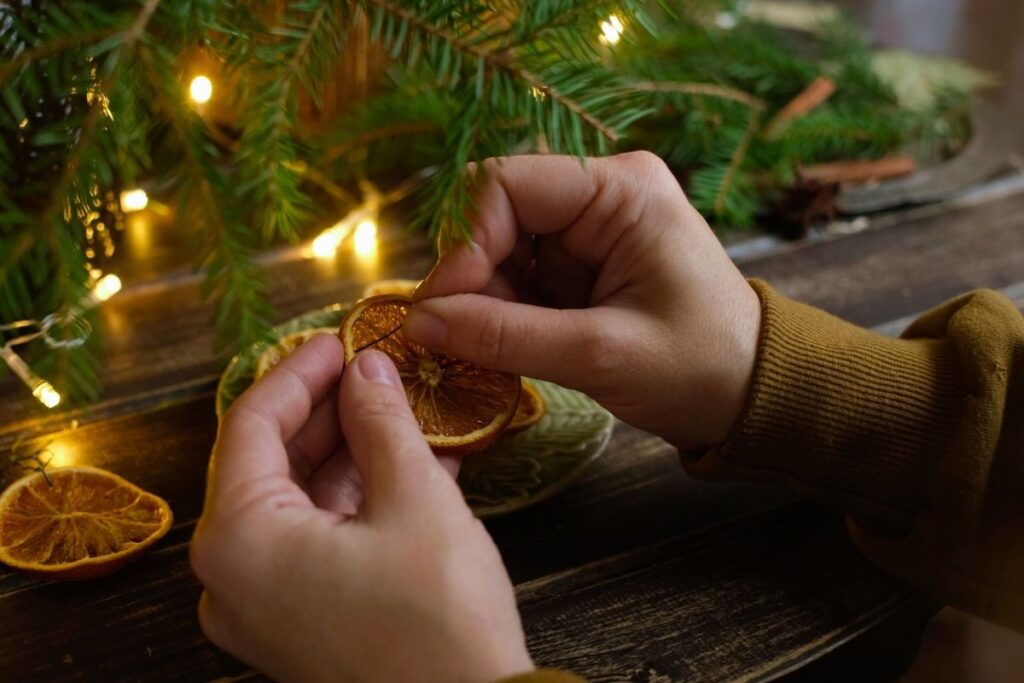 Hands making an eco-friendly DIY ornament made from a slice of dried orange.